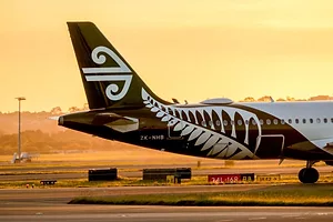AN AIRPLANE TAIL FIN AND BODY BEARING THE AIR NEW ZEALAND LOGO STANDS AGAINST A SUNSET