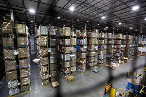 A FORKLIFT TRUCK DRIVES PAST HUGE STACKS OF GOODS IN A WAREHOUSE
