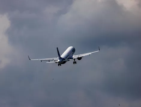 A white passenger airplane flying through a grey, cloudy sky