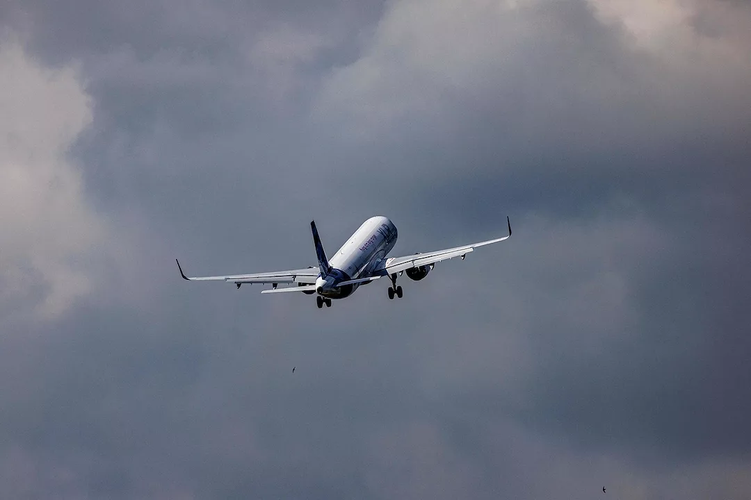 A white passenger airplane flying through a grey, cloudy sky