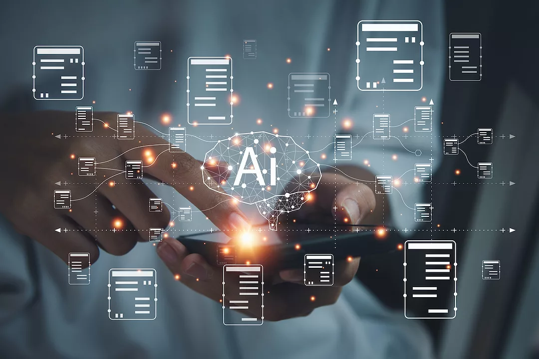 DIGITAL RENDERINGS OF CHARTS AND A BRAIN WITH THE LETTERS "AI" APPEAR ABOVE A CELL PHONE BEING HELD IN A PAIR OF HANDS.