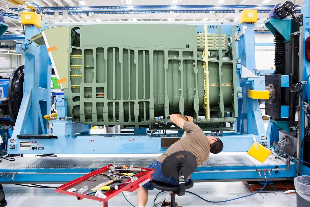 A WORKER LEANS OVER IN AN OFFICE CHAIR TO WORK ON A GIANT PIECE OF MACHINERY