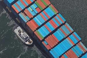 AN AERIAL SHOT OF A GIANT CONTAINER SHIP FLANKED BY A TUG MID-OCEAN