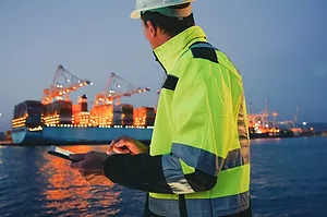 Man in protective gear holding tablet computer in front of harbor terminal at night