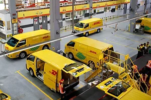 A DOZEN BRIGHT YELLOW VANS ARE ARRAYED IN A DISTRIBUTION CENTER, SEEN FROM ABOVE