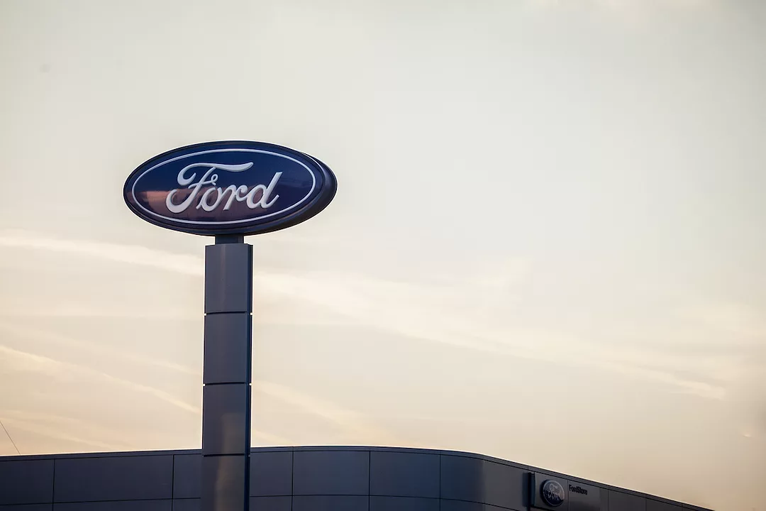 A FORD SIGN ABOVE A BUILDING CAN BE SEEN IN FRONT OF A YELLOW SKY.