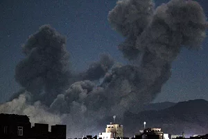 THICK PLUMES OF BLACK SMOKE RISE BEHIND A SERIES OF BUILDINGS, AT NIGHT