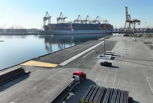 AN EMPTY WHARF STRETCHES ALONG A HARBOR, A LARGE CONTAINER SHIP IN THE BACKGROUND