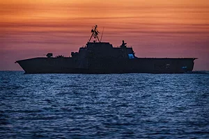 A warship at sea silhouetted at sunset