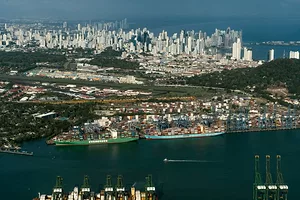 TWO SHIPS ARE DOCKED AT A PORT IN FRONT OF HILLS AND AN URBAN SKYLINE