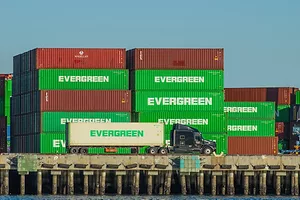 A semi-truck pulling a container next to a stack of other containers at the Port of Los Angeles