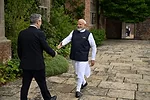 A MAN IN INDIAN CLOTHES WALKS TOWARDS A MAN IN A SUIT, HAND HELD OUT IN GREETING