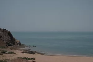 A rocky beach, with ships floating across a hazy horizon in the distance