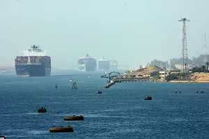 THREE LARGE CONTAINER SHIPS CAN BE SEEN TRAVELING ON A BODY OF WATER NEAR A SMALL HARBOR.