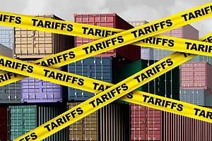 Yellow caution tape that reads "tariffs" arrayed across the foreground in front of stacks of multi-colored shipping containers