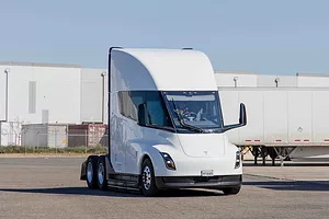 A white semi-truck cab parked in a lot with white metal buildings in the background